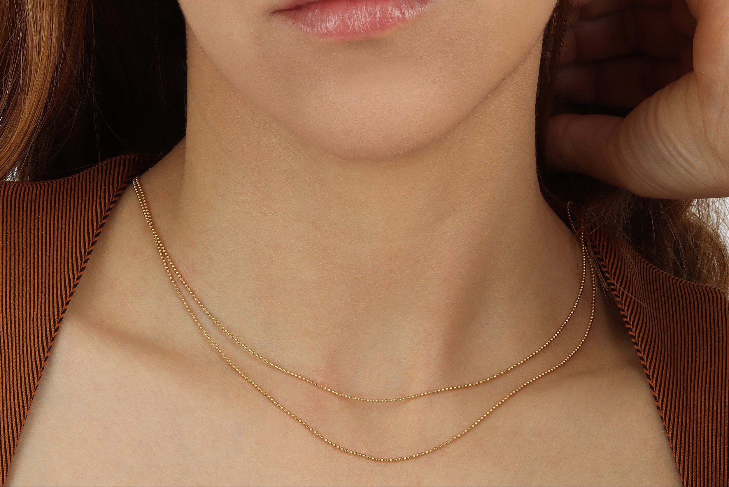 A girl model wearing 16 inch, 18 inch, and 20 inch 1.0mm Ball chain solid 14K Yellow Gold on plain white background with detailed product shot Made in Italy